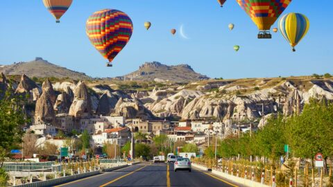 Hot air balloons fly over the Goreme road at sunrise in Cappadocia